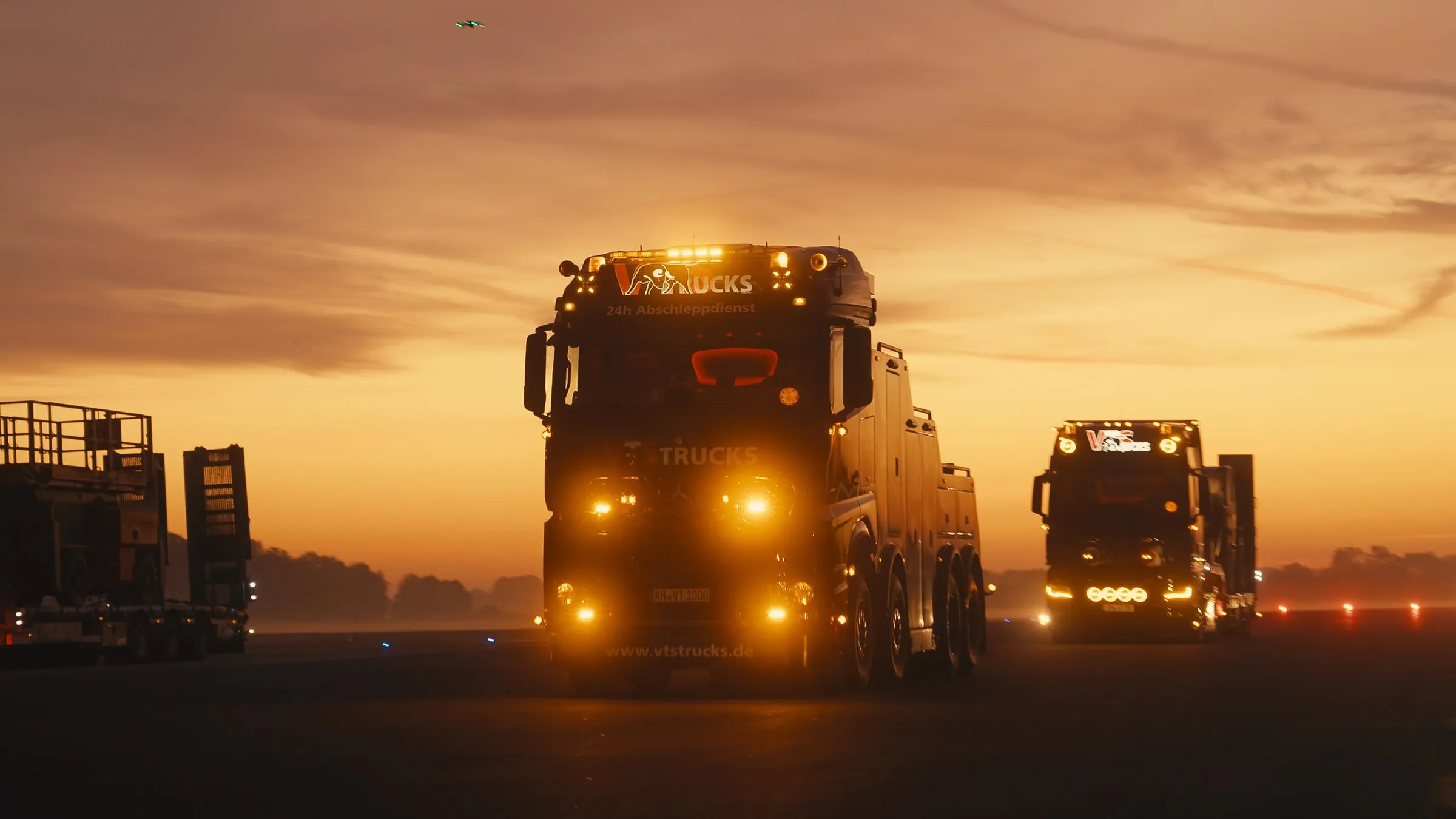 Lkw-Kolonne mit Scheinwerfern kommt im Abendlicht auf der Straße entgegen
