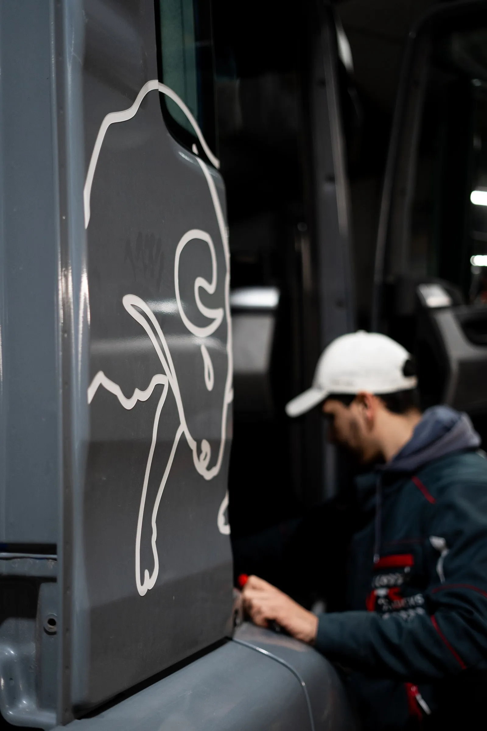 Mitarbeiter mit Kappe arbeitet an der Fahrertür eines Lkw mit Bullen-Grafik