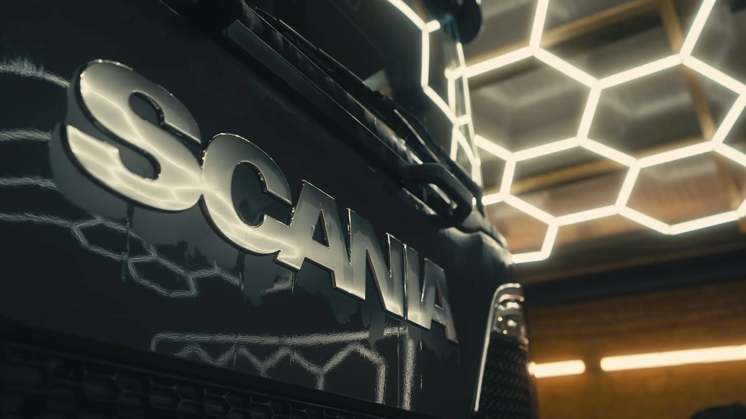 Nahaufnahme des Scania-Schriftzugs am Kühlergrill unter Wabenleuchten