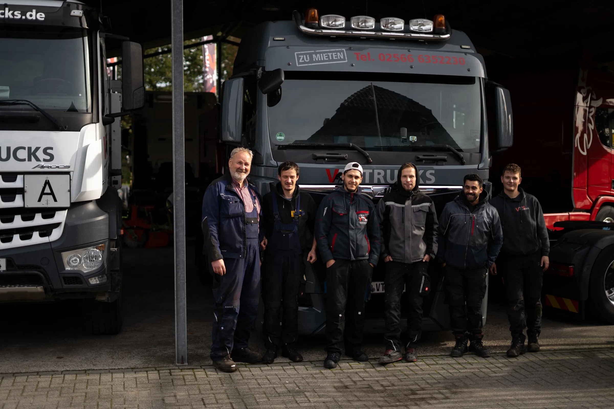 Das Team der VTS Trucks GmbH steht in Arbeitskleidung vor Lkw an der Halle