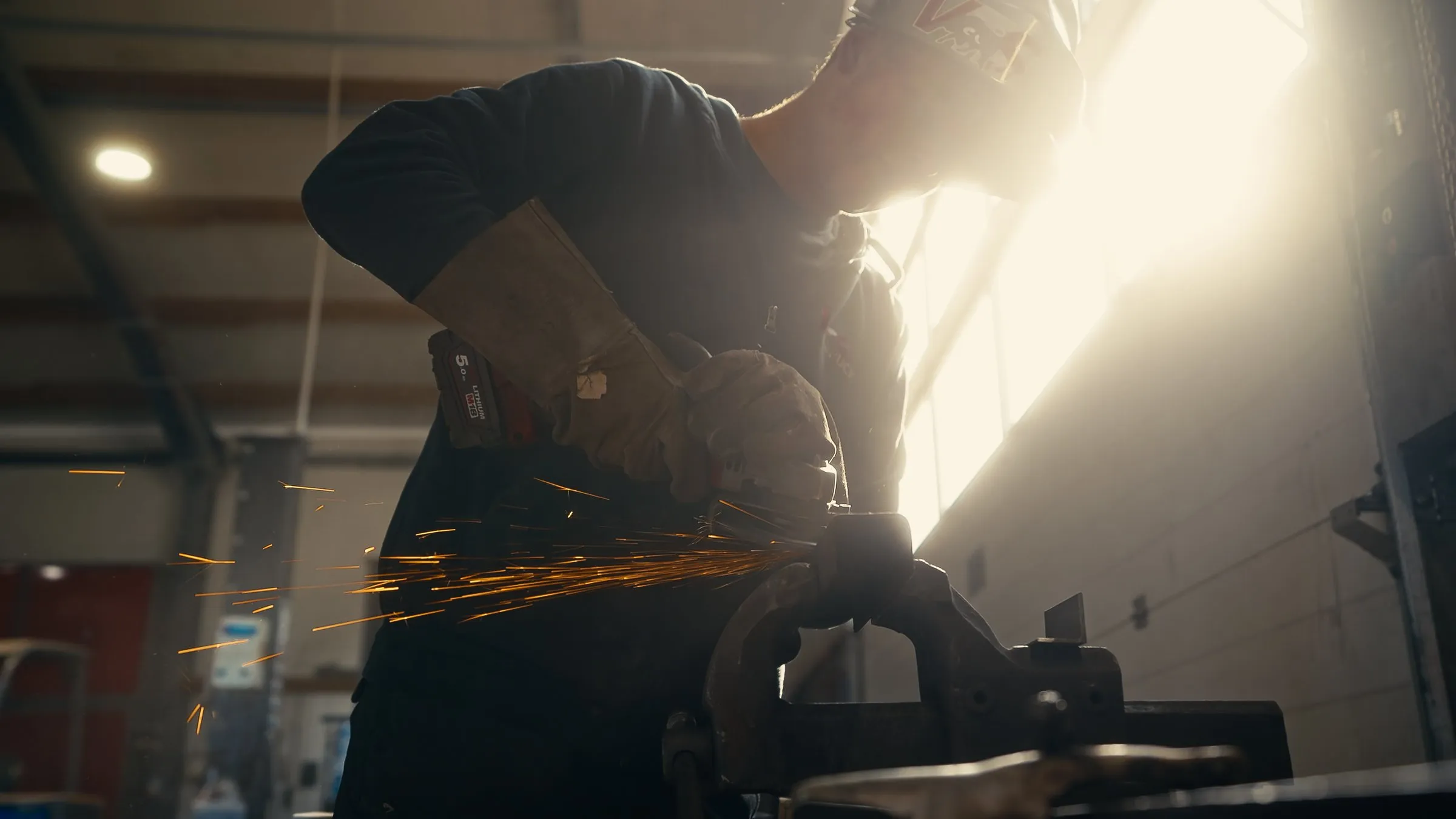 Mitarbeiter schleift ein Metallteil in der Werkstatt, Funken im Gegenlicht